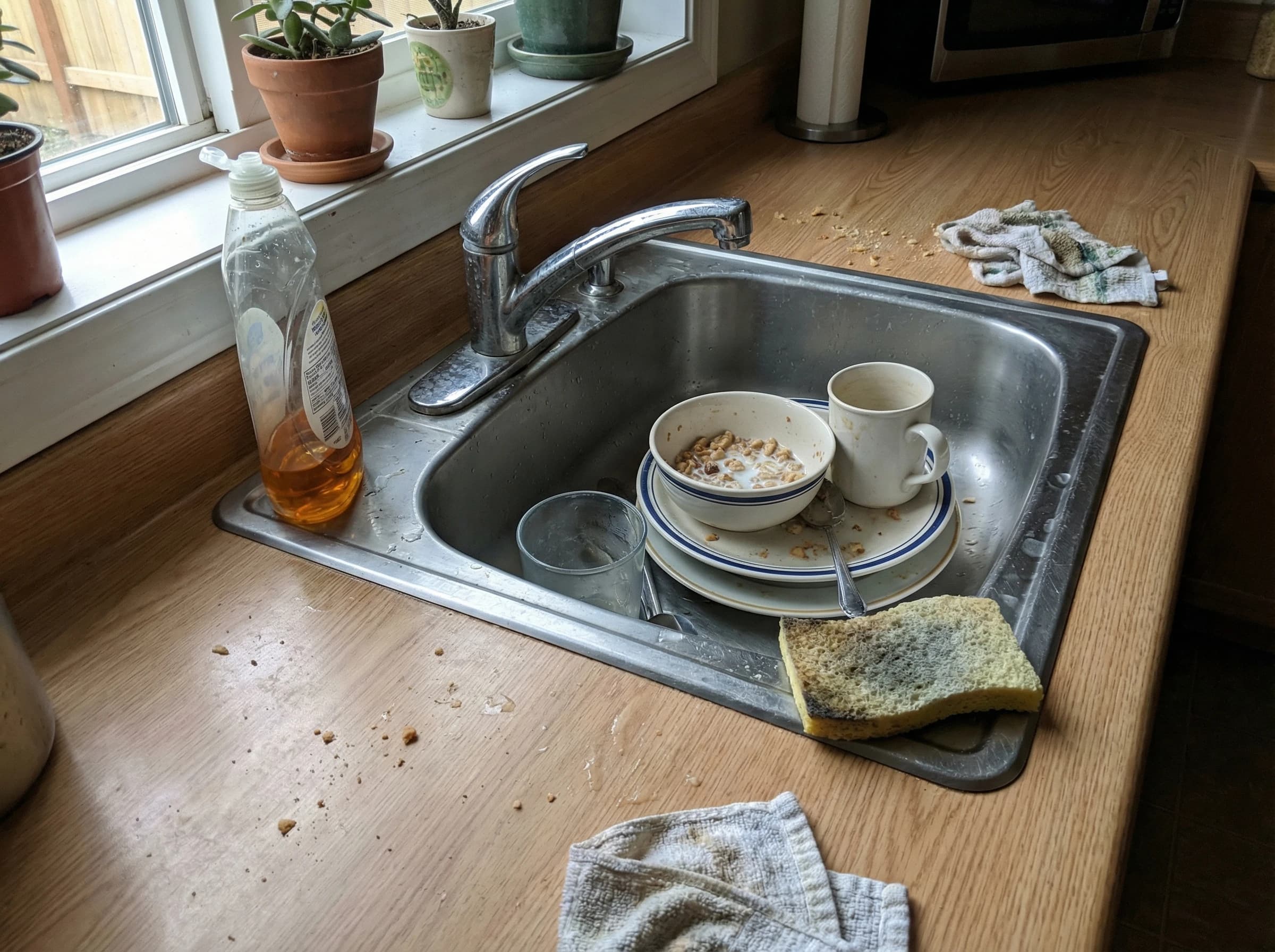Dirty dishes pile up in kitchen sink, countertop messy with food debris