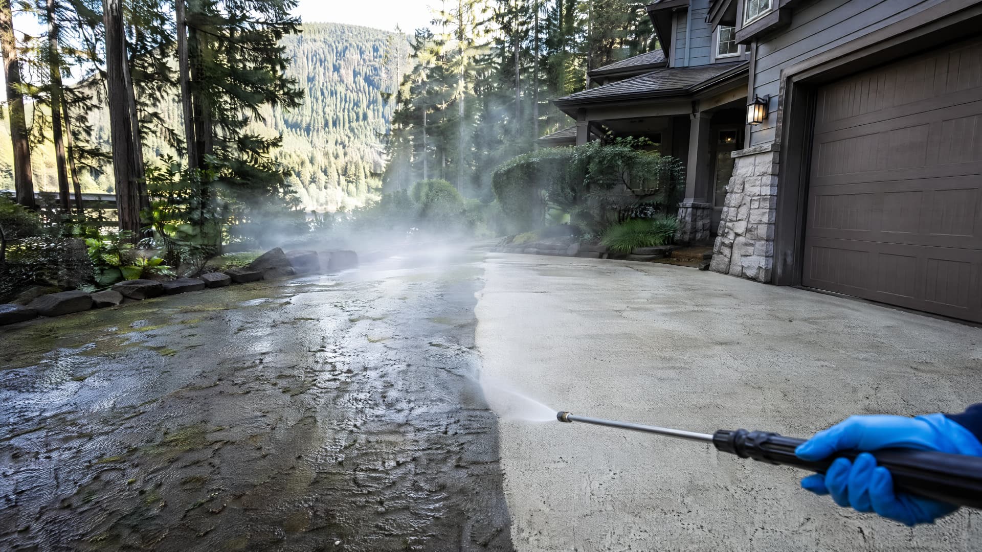 Half-cleaned North Vancouver driveway mid pressure wash, grime on one side and pale clean concrete on the other, mountains behind