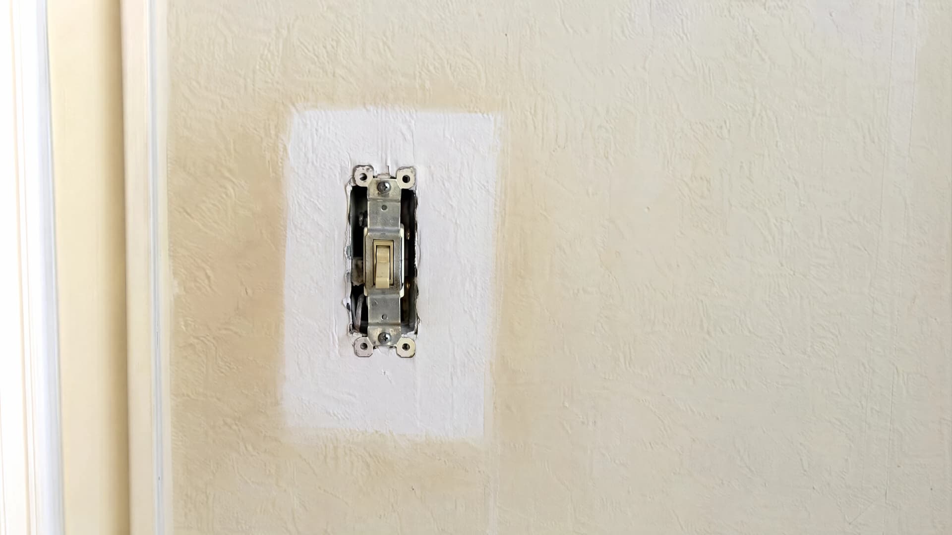 Close daylight view of a wall corner and light switch plate showing a faint yellow nicotine tinge against clean paint