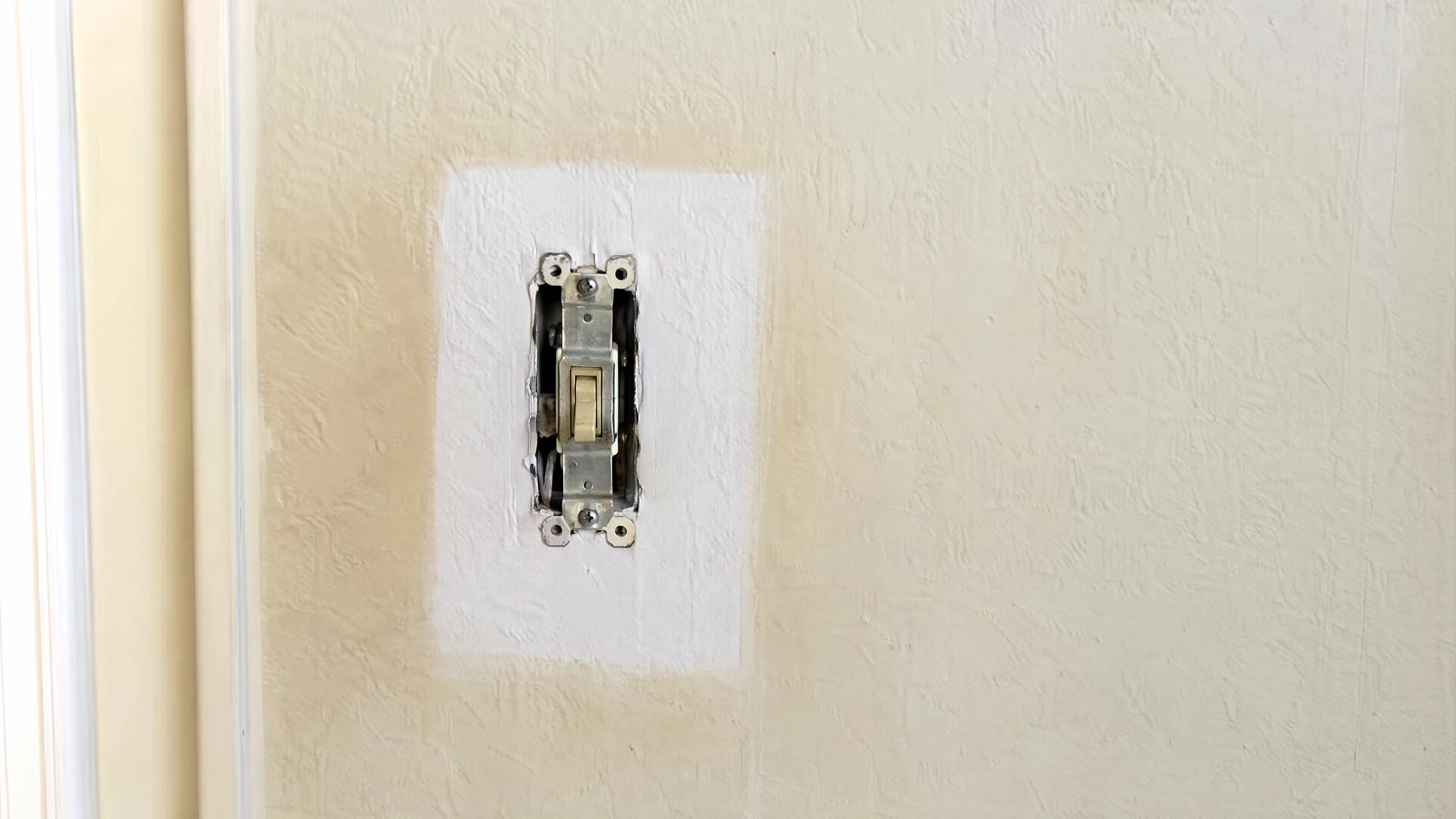 Close daylight view of a wall corner and light switch plate showing a faint yellow nicotine tinge against clean paint