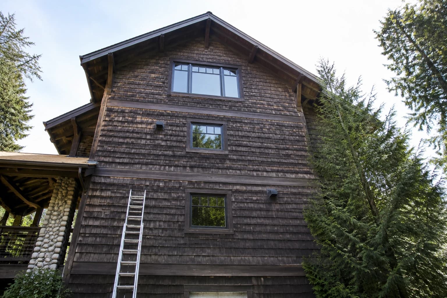 Three-storey West Coast cedar-shingled house seen from the ground, an extension ladder reaching only the second floor