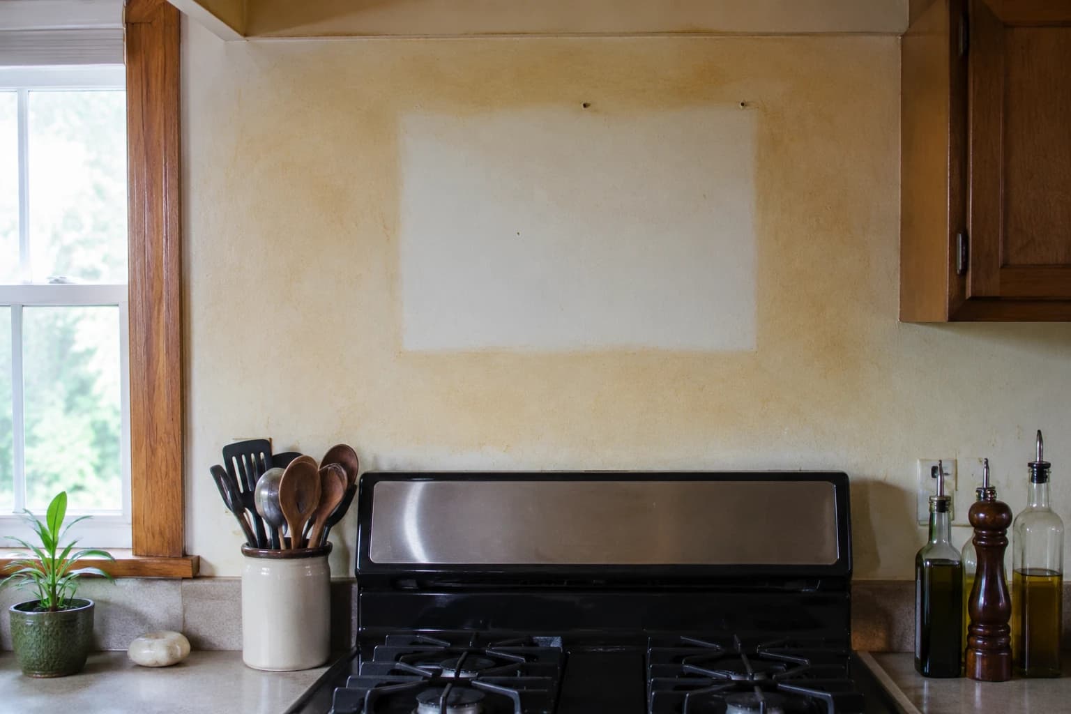 Amber protein film yellowing a kitchen wall above the stove, with a clean rectangle where a frame hung