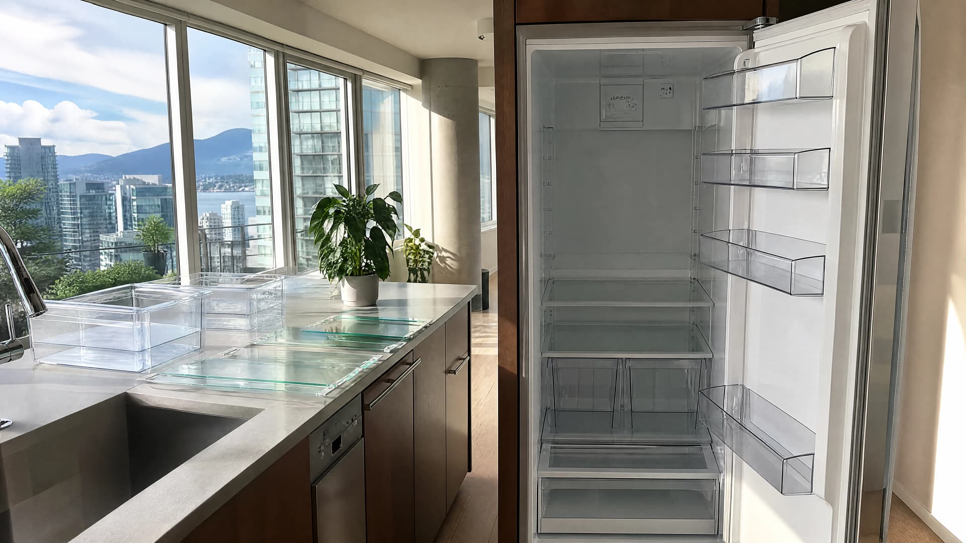 Empty spotless refrigerator standing open in a bright Vancouver condo kitchen, glass shelves drying on the counter