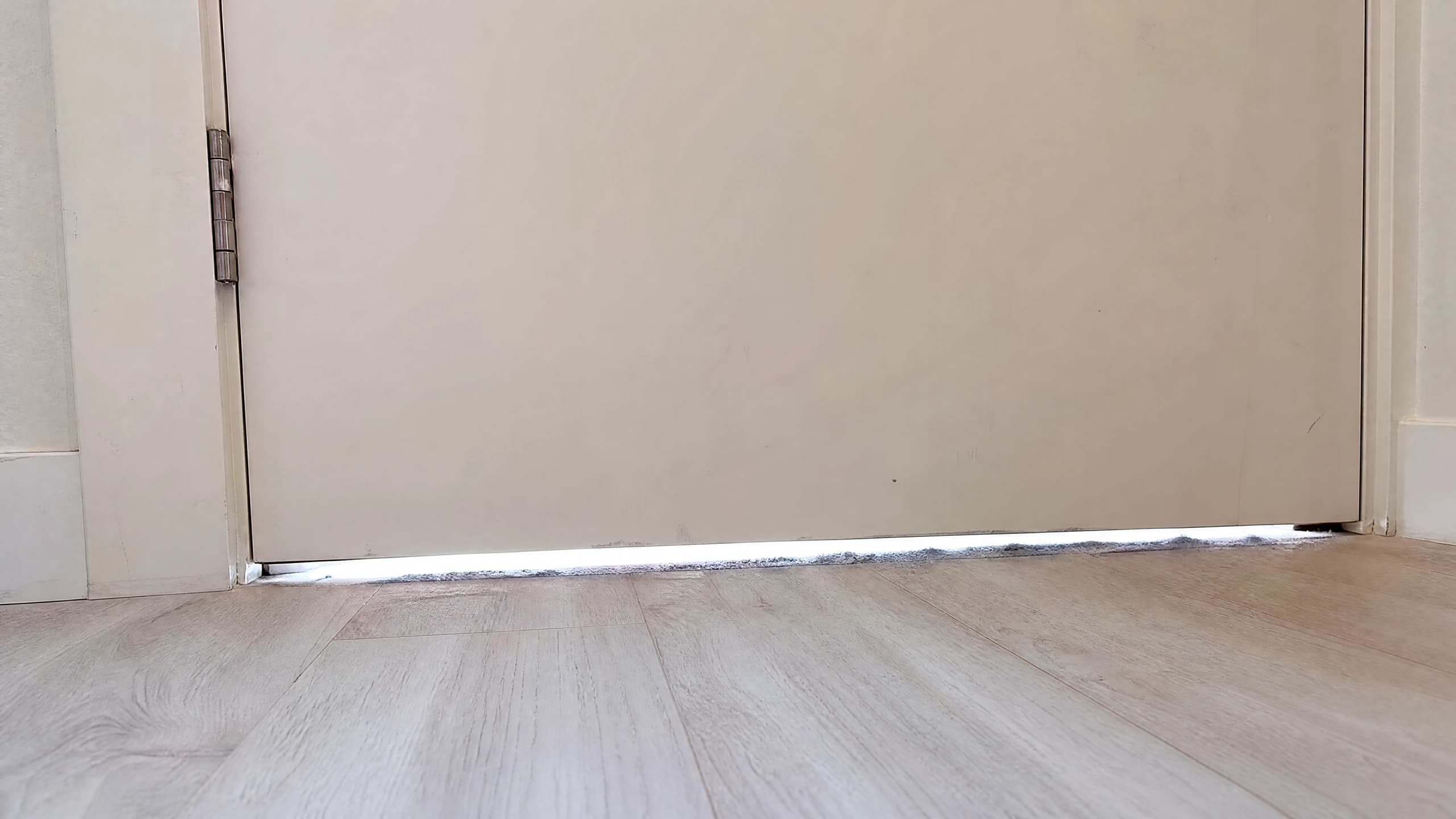 Daylight glowing under a condo suite entrance door with a grey dust line settled along the threshold