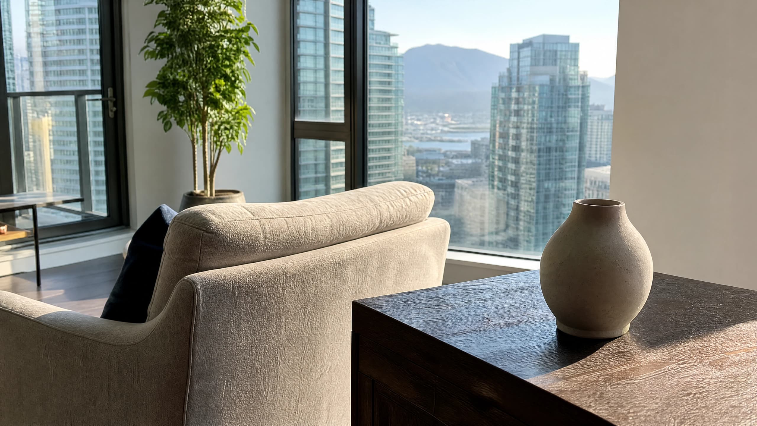 Morning light rakes across a dusty dark side table in a Vancouver high-rise condo with the North Shore mountains beyond