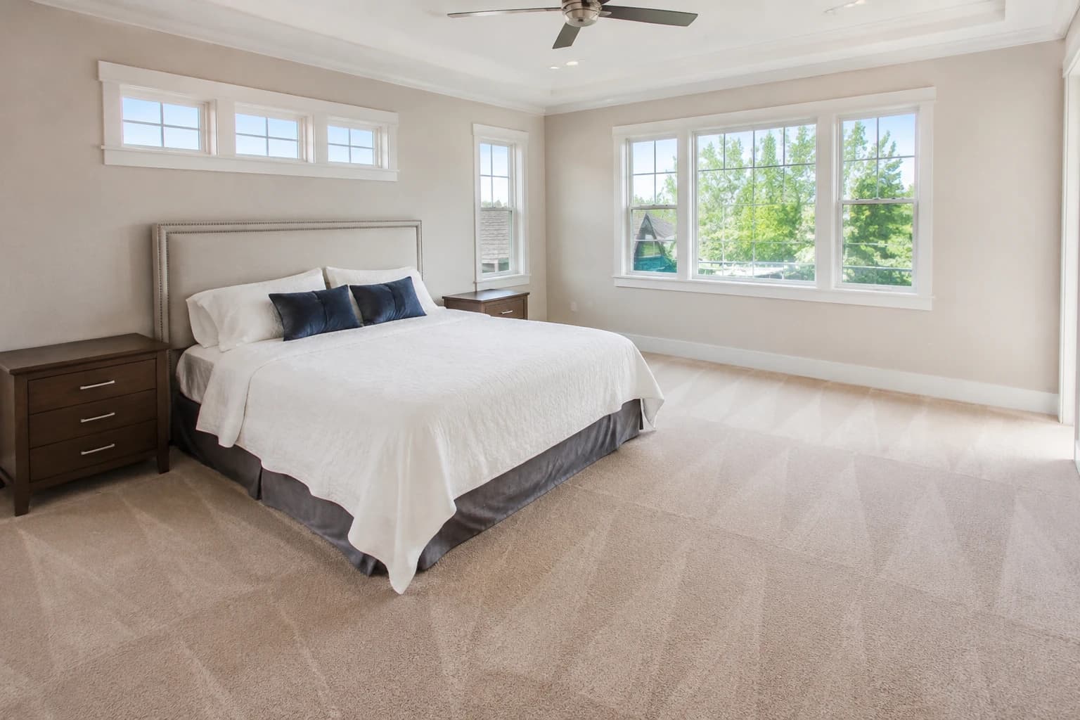 Tidy main bedroom in a three-bedroom home with a crisply made bed and fresh vacuum lines across the floor